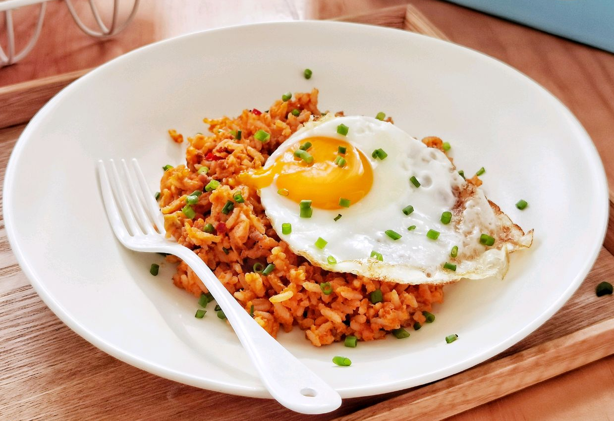 Serve kimchi fried rice with fried egg on top, garnished with green onions.