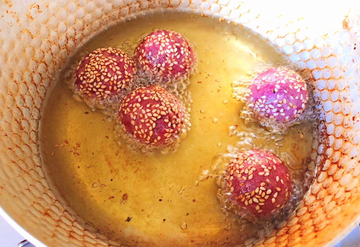 Frying purple sweet potato balls in hot oil, stirring to prevent sticking.