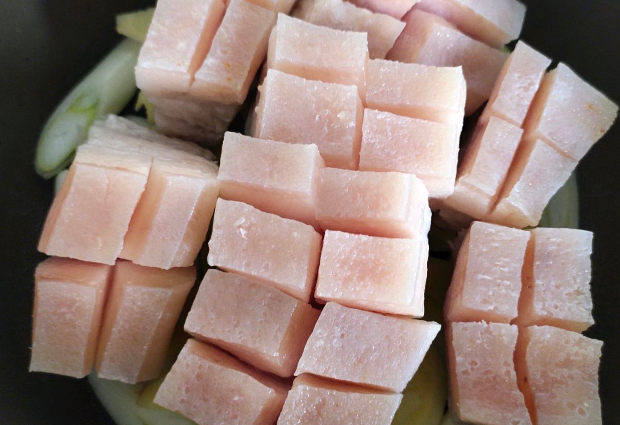 Layer pork belly on top of onions and ginger in pot for cooking.