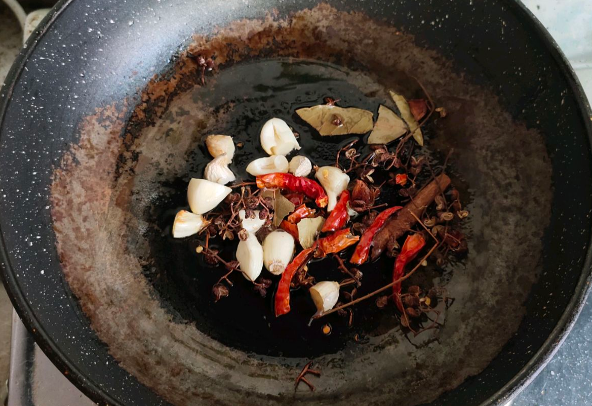 Heat oil, stir-fry garlic with spices (star anise, Sichuan peppercorns, chili peppers, bay leaves) for Big Plate Chicken.