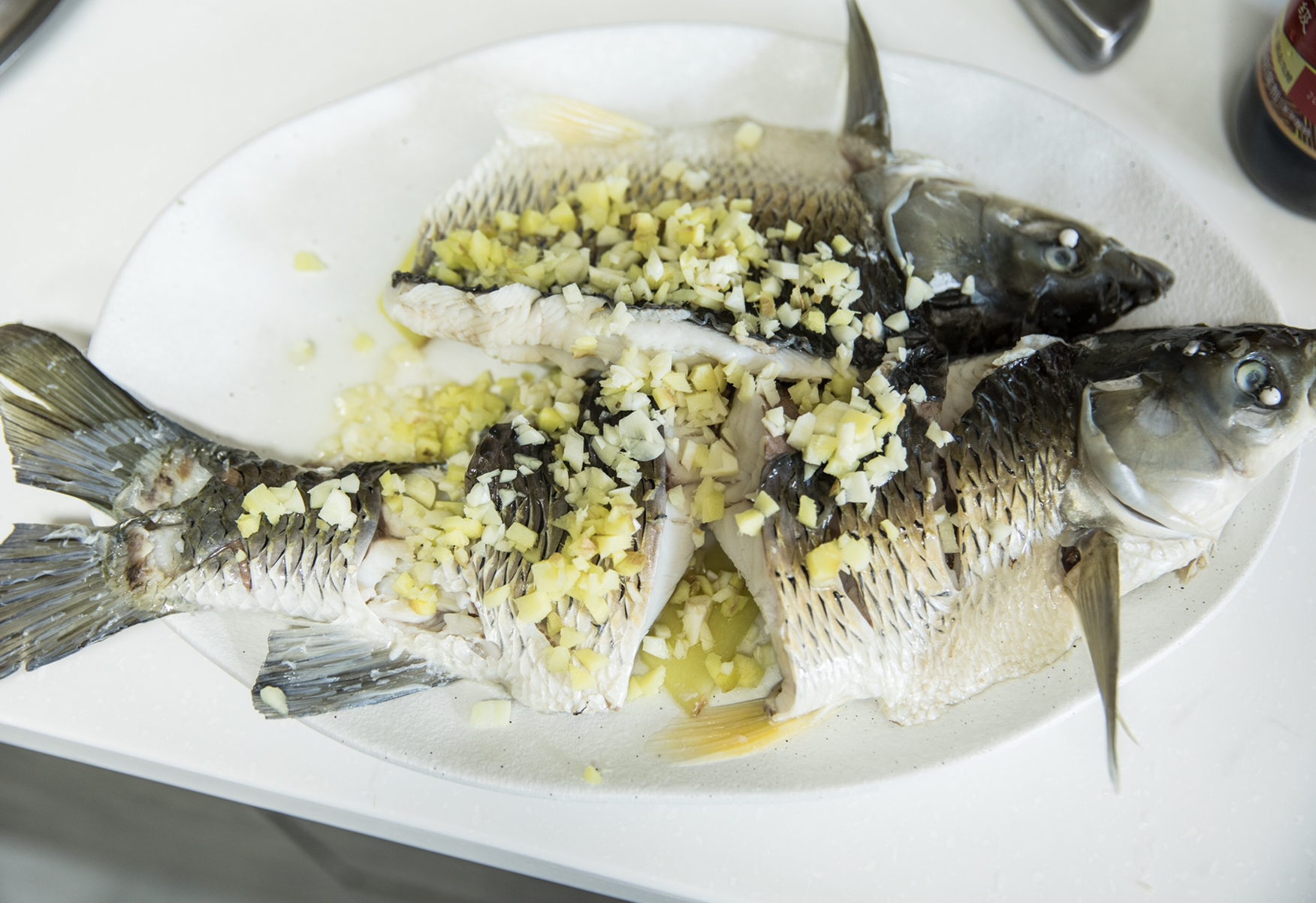 Steamed grass carp removed from pot, garnished with 10g of minced ginger and garlic.