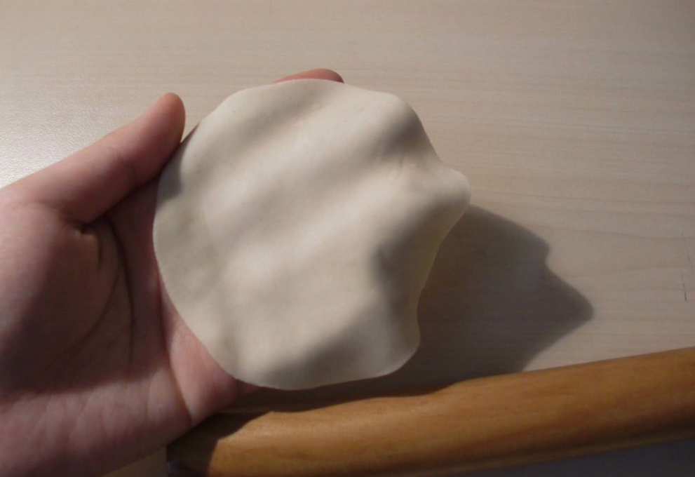 Roll dough into a round wrapper with varying thickness.