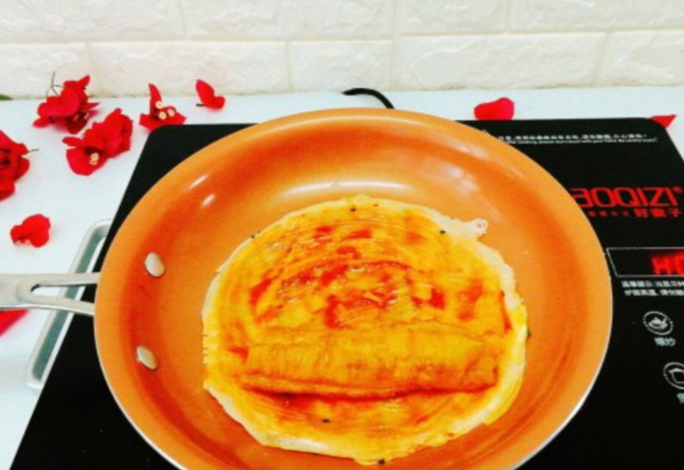 Brush pancake with tomato sauce, place youtiao on top. Flip pancake quickly and gently to avoid breaking it. (77 characters)