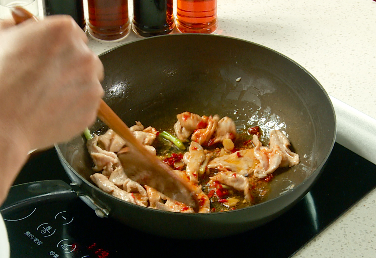 Add aromatics and chili by frying scallions, ginger, and chili peppers with pork.