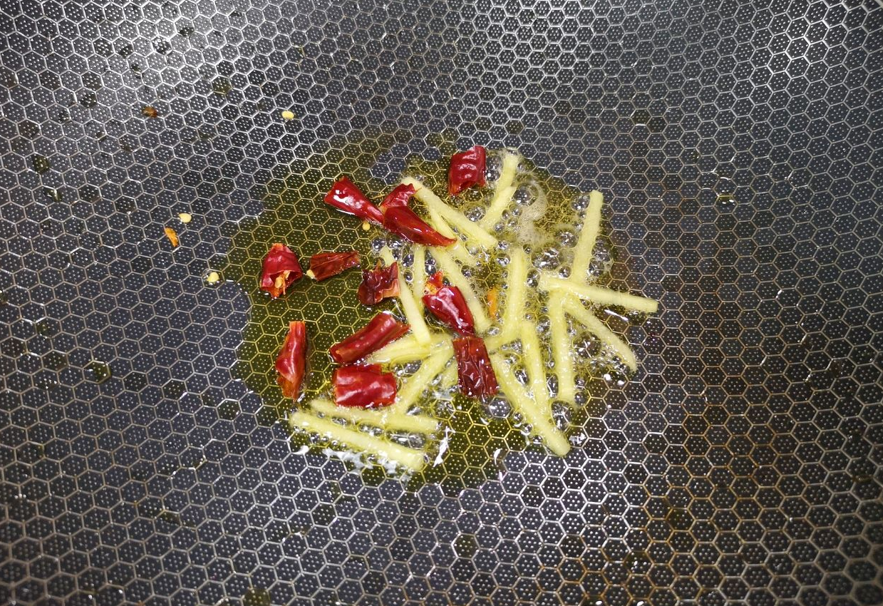 Heat oil in pan, sauté ginger strips and dried chili peppers until fragrant.