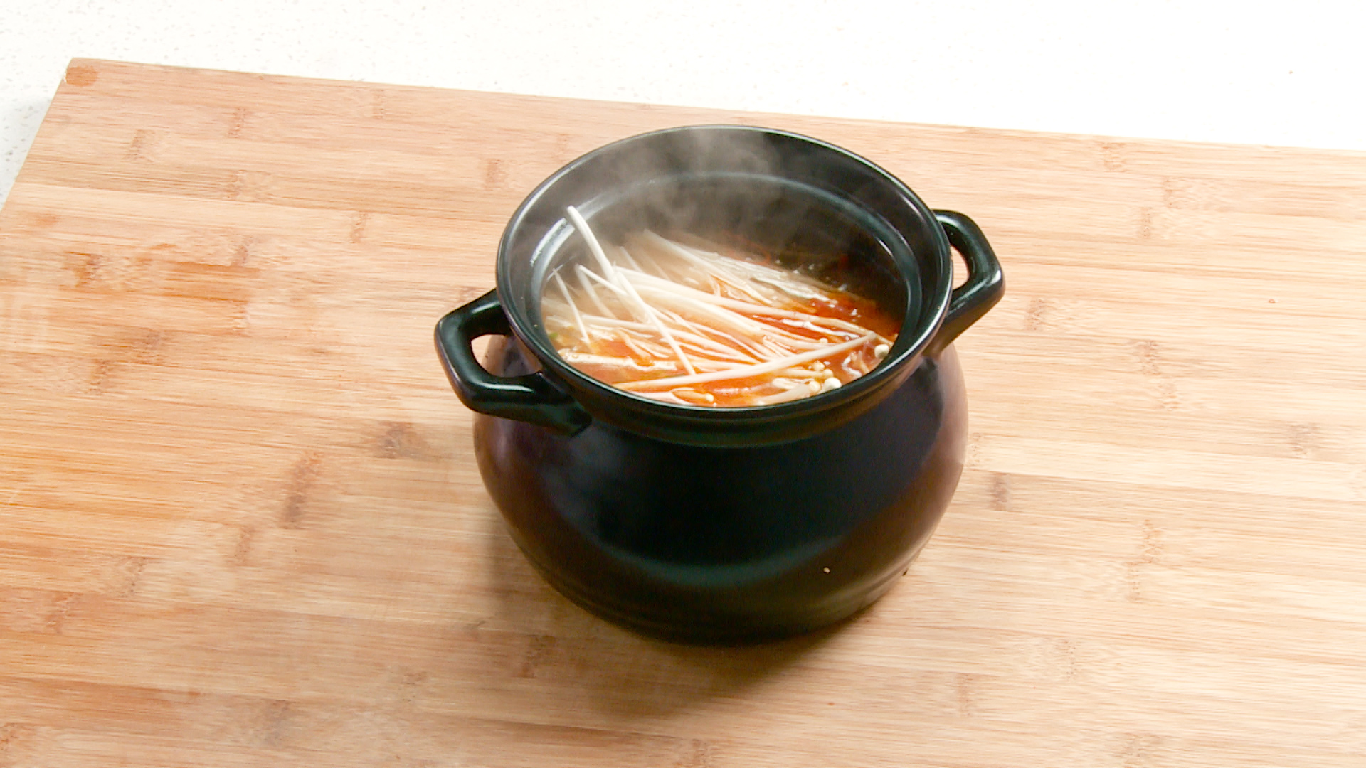 Transfer stir-fried mixture to clay pot, add water, salt, chili powder, boil, add enoki mushrooms, simmer. Clay pot care tip included.