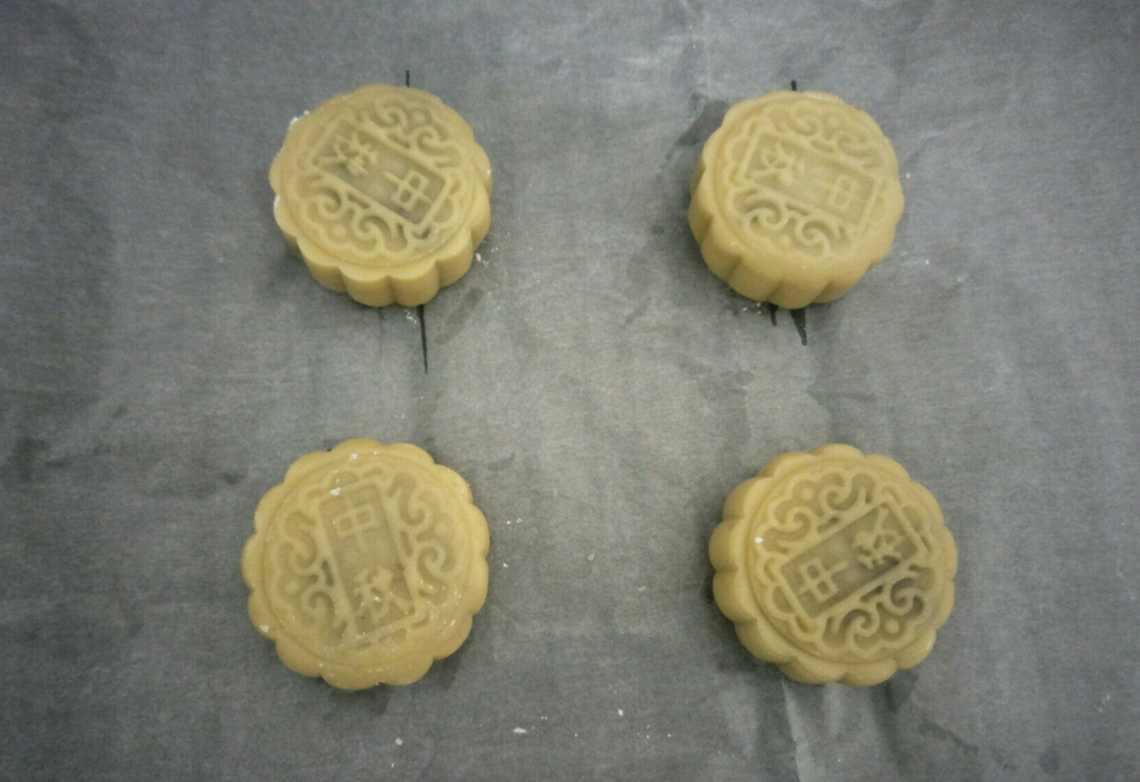 Shape mooncakes, sprinkle water, bake at 170°C for 5 mins to set. Non-stick tray may not need parchment paper.