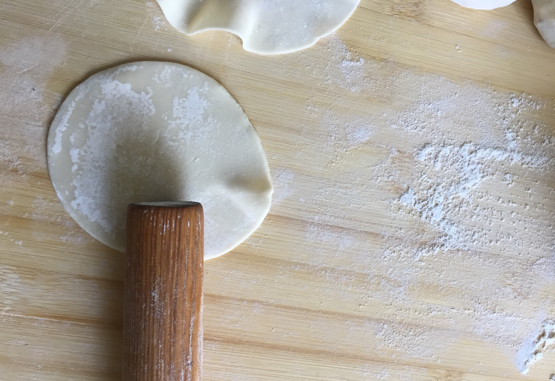 Roll dumpling wrappers' edges using a rolling pin to prepare for filling.