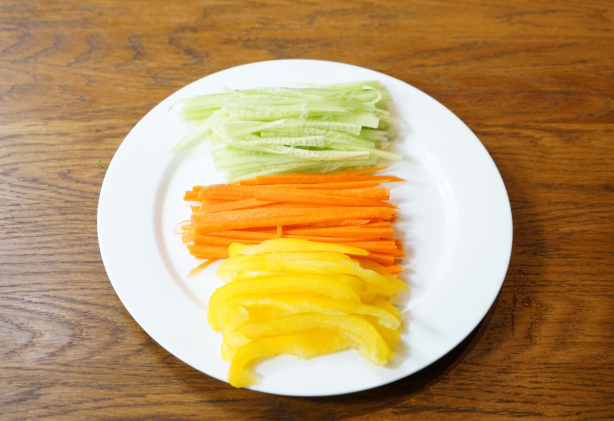 Wash and prepare cucumber, carrots, and bell pepper. Julienne and slice, then arrange on plate.