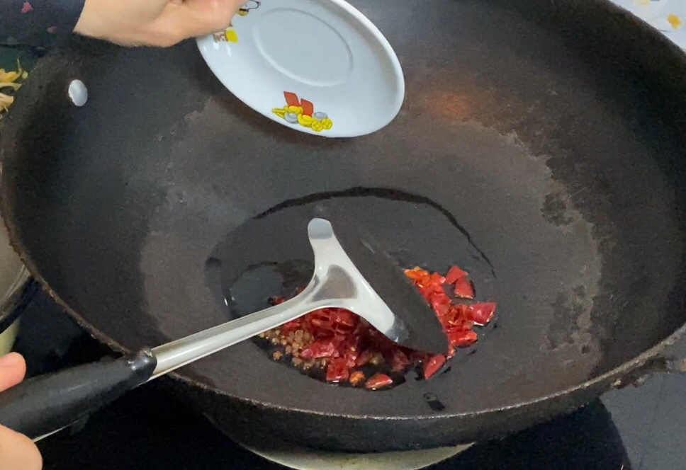 Fry dried chili peppers and Sichuan peppercorns in hot oil in a wok, then set them aside. Use any wok you have.