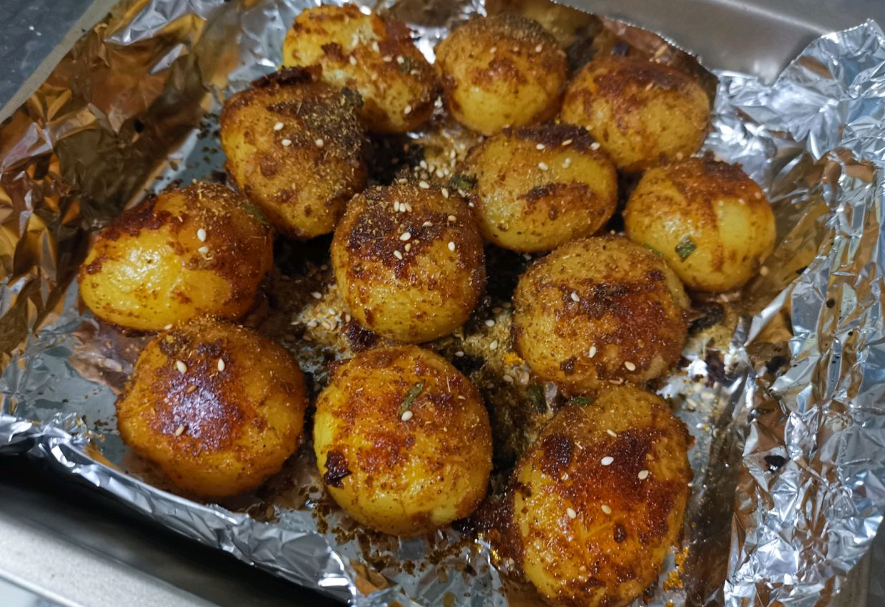 Bake potatoes, sprinkle with cumin, sesame seeds for spicy, crispy roast potatoes.