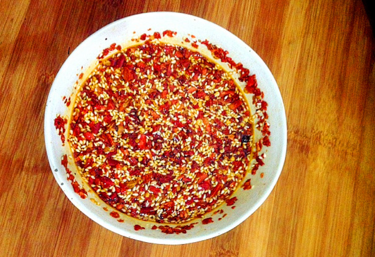 Hot oil is poured over chili powder and sesame seeds in a bowl.