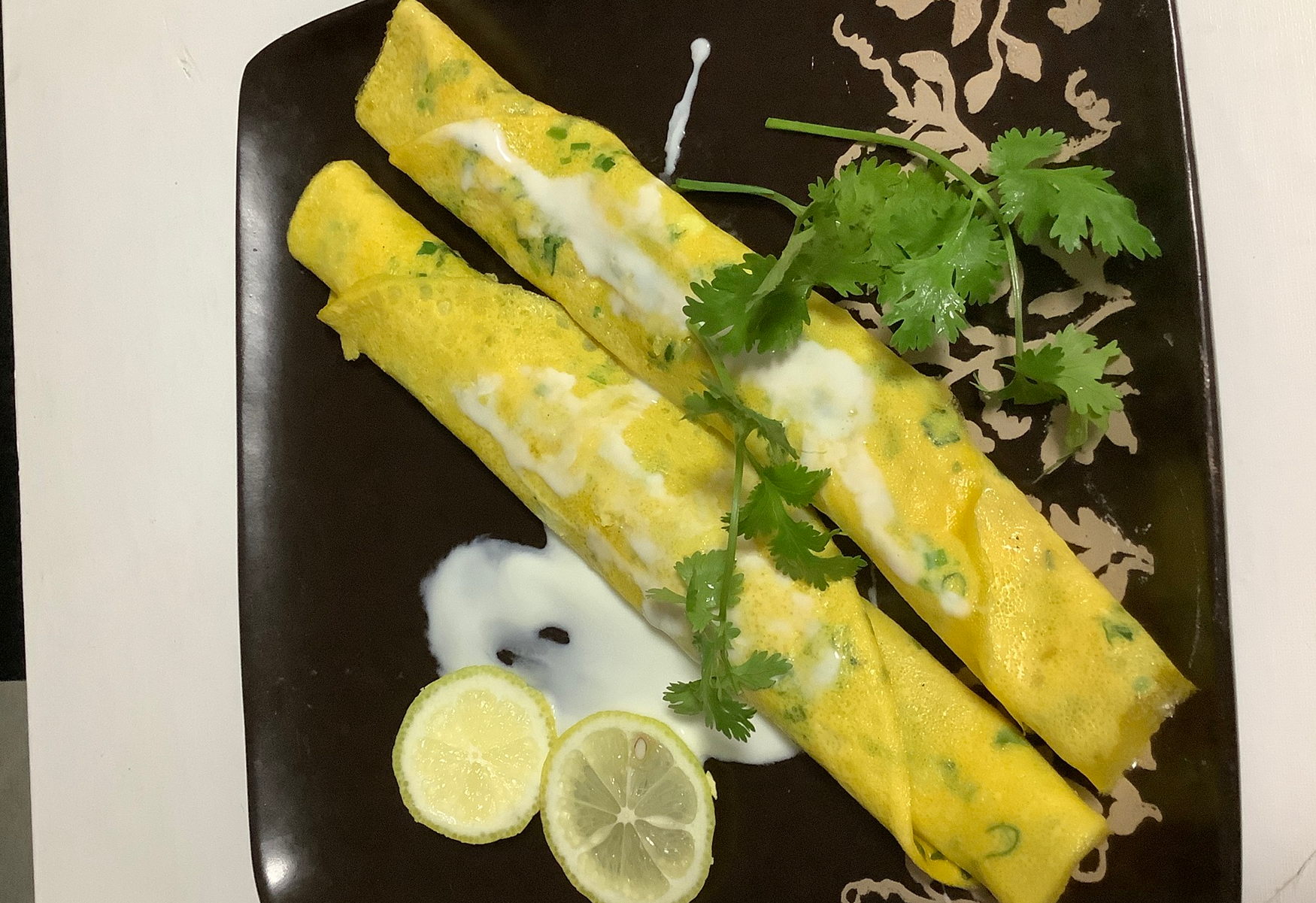 Roll omelette, garnish with yogurt, cilantro, lemon.