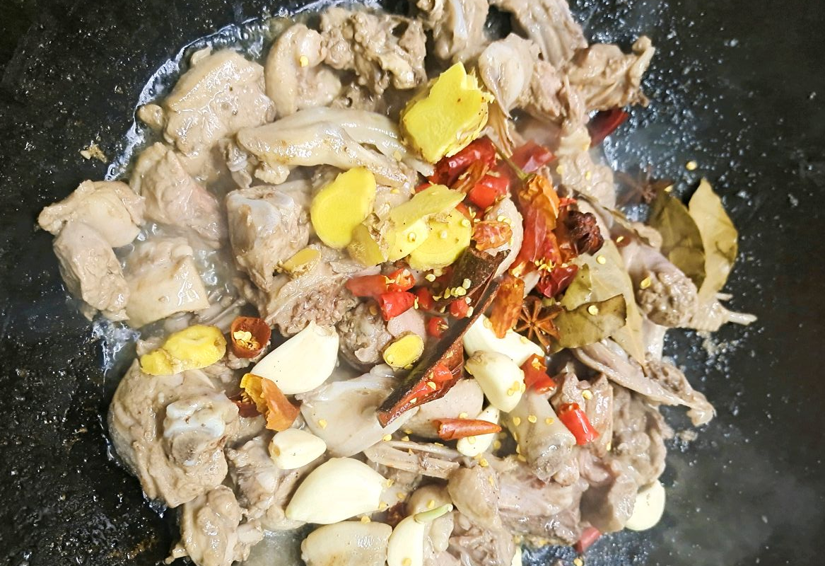 Stir-fry ginger, garlic, cinnamon, star anise, bay leaves, and chili peppers in a pan.