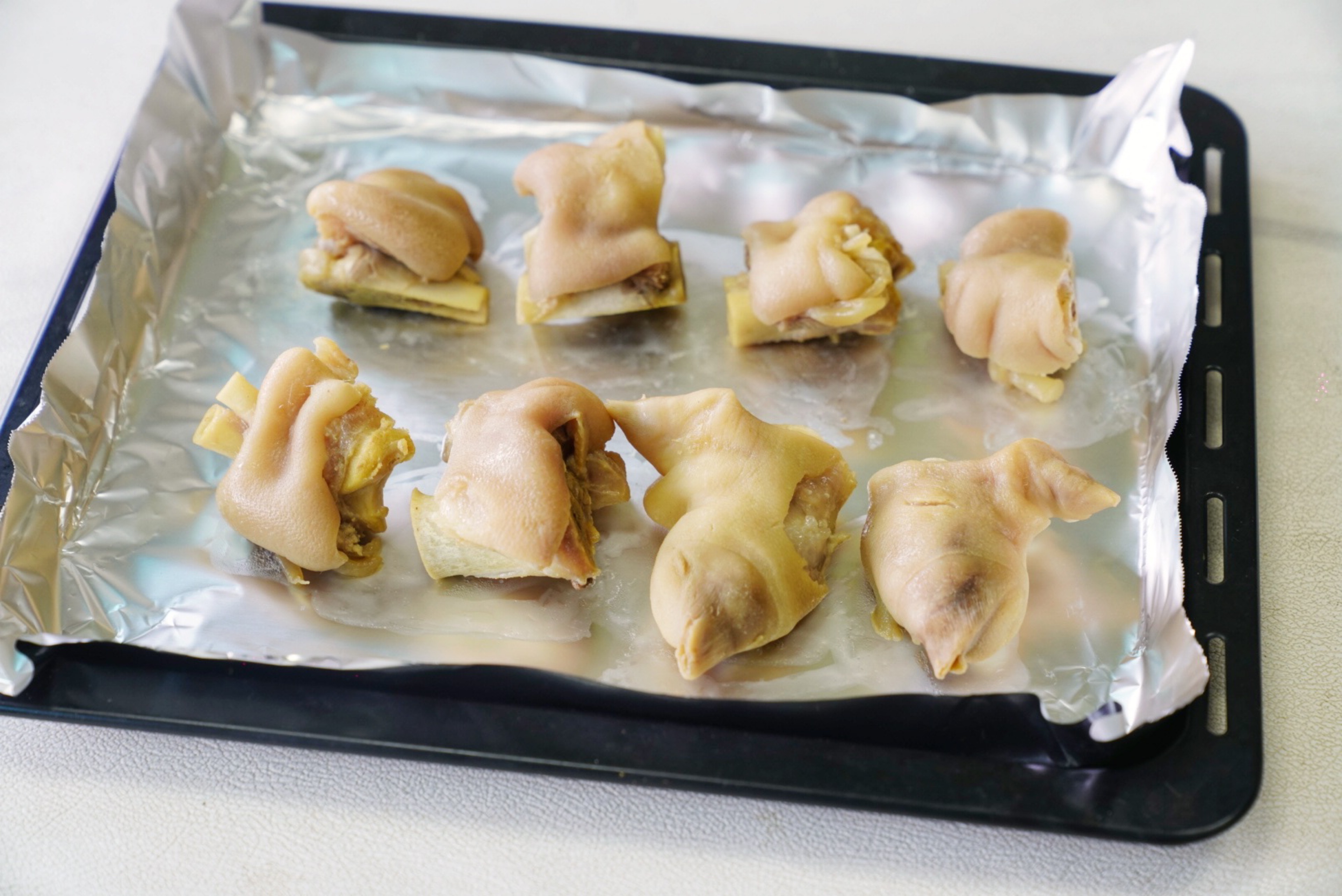 remove, rinse, and neatly arrange the pigs' trotters in a baking tray